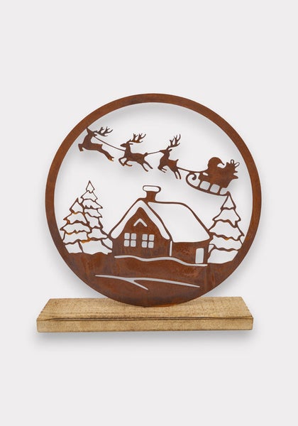 Dekorative Weihnachtsszene aus Metall mit Haus, Tannenbäumen, Rentieren und Weihnachtsmann im Schlitten auf Holzsockel