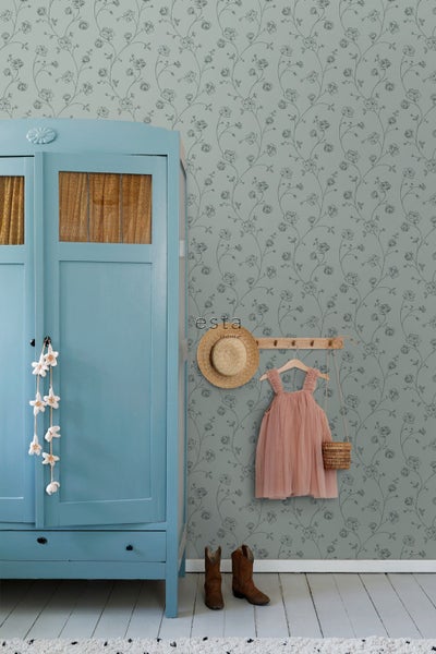 Zimmer mit floraler Tapete, blauem Holzschrank, Hakenleiste mit rosa Kleid und Hut, braunen Stiefeln und esta home Logo.