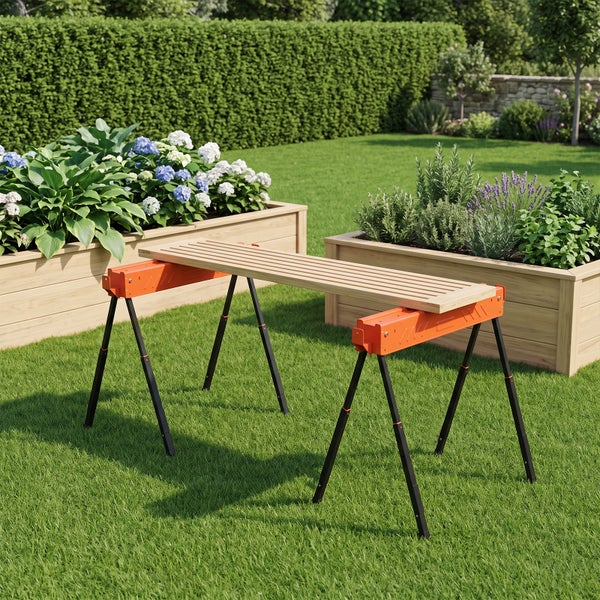 Zwei höhenverstellbare Arbeitsböcke mit einer aufgelegten Holzlatte als provisorischer Tisch im Garten vor zwei Holzhochbeeten.