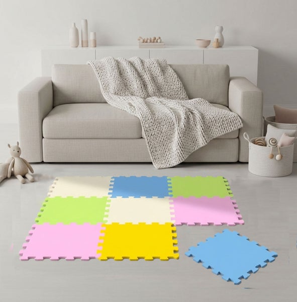 Farbenfrohe Schaumstoff-Puzzlematte auf einem Wohnzimmerboden vor einem Sofa mit ineinandergreifenden quadratischen Teilen.