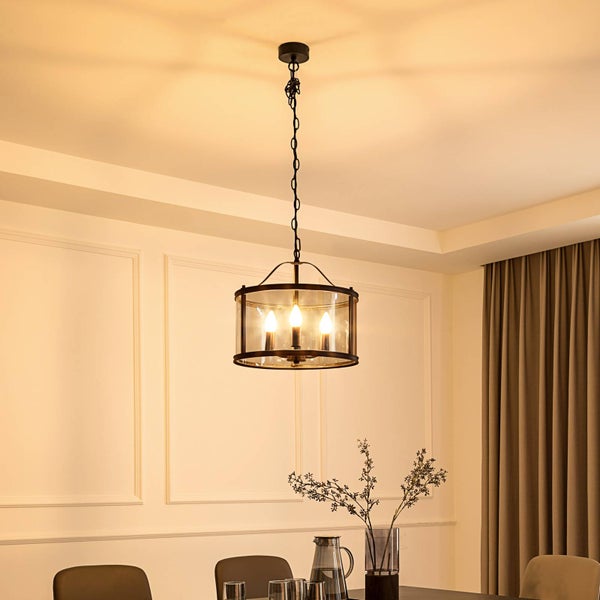 Schwarze Pendelleuchte aus Metall und Glas mit drei Leuchtmitteln in einem hellen Esszimmer mit Wandleisten und Vorhängen.