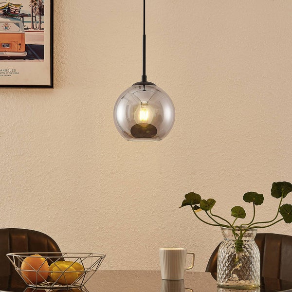 Helle, organisierte Innenszene mit einer modernen Pendelleuchte mit kugelförmigem Glasschirm über einem Tisch mit Obstschale, Tasse und Pflanze.