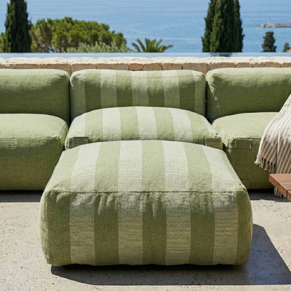 Grün gestreiftes modulares Outdoor-Sofa und Hocker auf einer hellen Terrasse mit Meerblick.