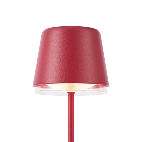 Nahaufnahme einer modernen Tischleuchte mit rotem Lampenschirm und warmem Lichtschein.
