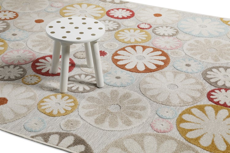 Kinderteppich mit bunten kreisförmigen Blumenmotiven und ein weißer Hocker mit goldenen Punkten.