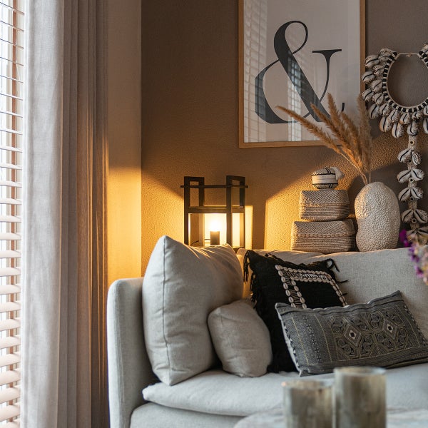 Wohnbereich mit gemütlichem Sofa, Dekoobjekten und einer modernen Tischleuchte vor einer Wand mit Bild.