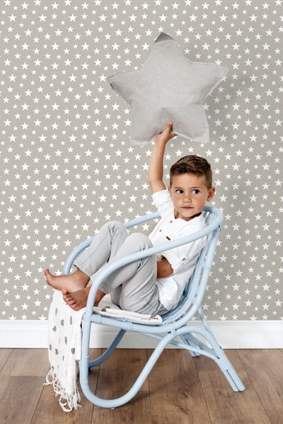 Junge sitzt in einem blauen Rattansessel vor einer Wand mit Sternentapete und hält ein Sternkissen hoch