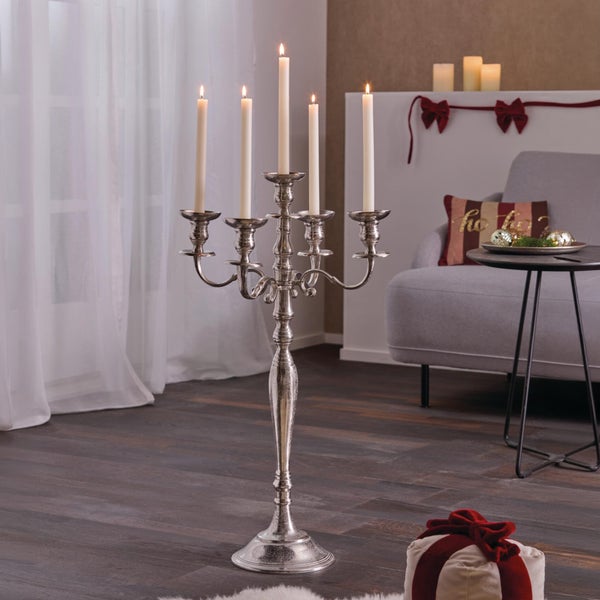 Fünfarmiger silberfarbener Kerzenleuchter aus Metall auf einem Holzboden in einem weihnachtlich dekorierten Wohnzimmer.