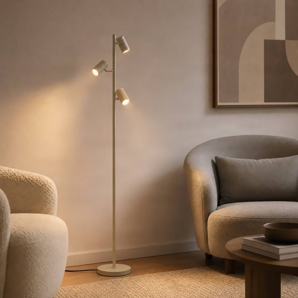 Moderne Stehlampe mit drei schwenkbaren Strahlern in einem gemütlich eingerichteten Wohnzimmer mit Sesseln und Beistelltisch.