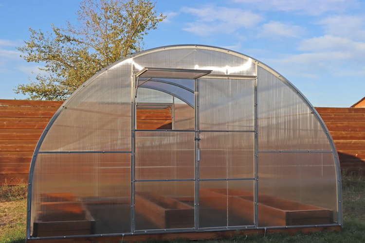 Rundbogen-Gewächshaus aus Polycarbonat mit Metallrahmen, Tür und Fenster, inklusive Hochbeeten im Innenraum.