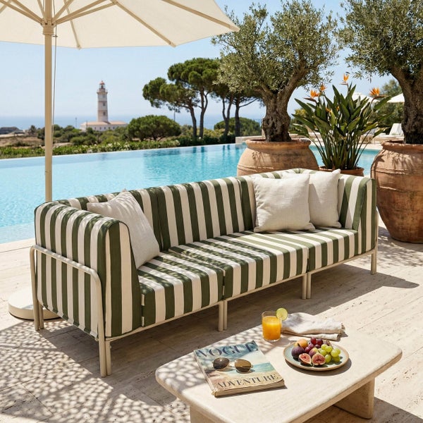Modernes Outdoor-Sofa mit grün-weiß gestreiften Kissen auf einer hellen Terrasse am Pool mit Gartenmöbeln und Meerblick.