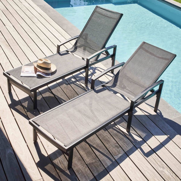 Zwei moderne Sonnenliegen mit Metallgestell und Textilbespannung auf einer Holzterrasse neben einem Pool.