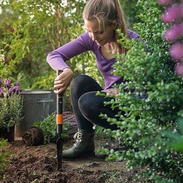 Eine Frau benutzt einen Pflanzlochstecher im Garten, um ein Loch für eine neue Pflanze zu machen.