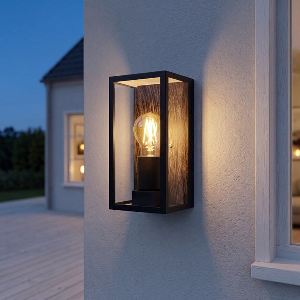 Rechteckige Außenwandleuchte mit schwarzem Metallrahmen, Glaseinsätzen und Rückwand in Holzoptik, montiert an einer Fassade bei Dämmerung.