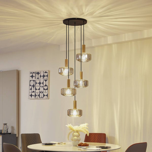 5-flammige Pendelleuchte mit Glasschirmen und goldfarbenen Fassungen über einem Esstisch, erzeugt ein radiales Lichtmuster an der Zimmerdecke.