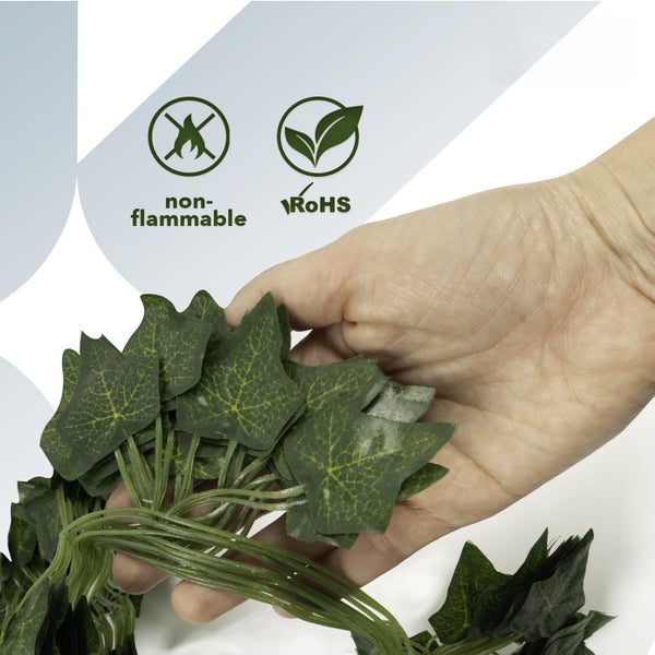 Hand hält künstliche Efeuranken mit Symbolen für schwer entflammbar und RoHS-konform.