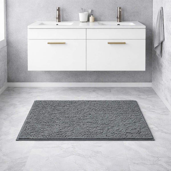 Graue Badematte mit Struktur auf einem hellen Fliesenboden vor einem weißen Doppelwaschtisch im modernen Badezimmer.