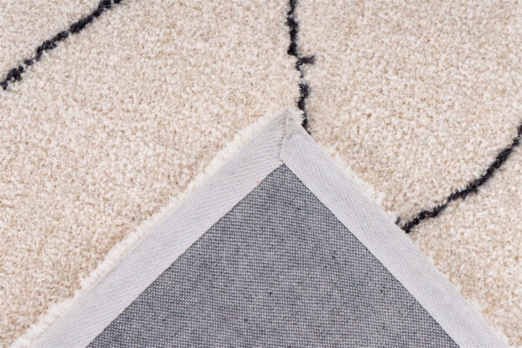 Nahaufnahme eines Teppichs mit Flor, Linienmuster und umgeschlagener Ecke, die die gewebte Rückseite mit Stoffkante zeigt.