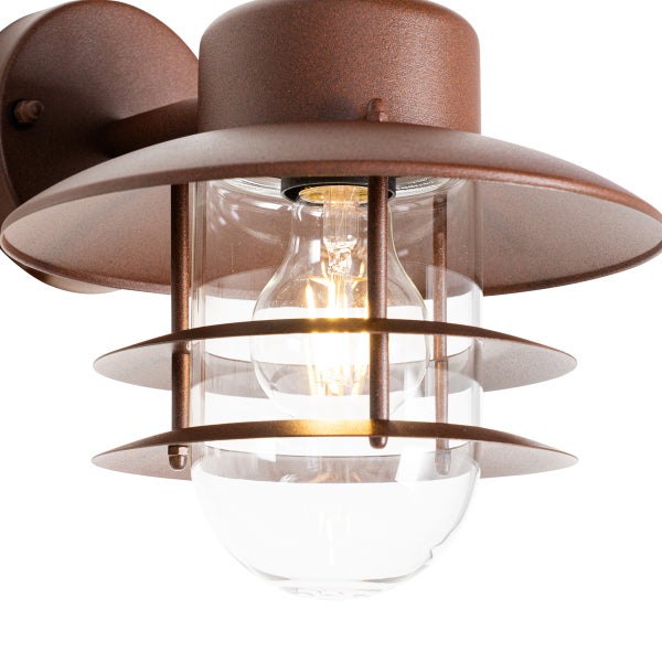 Rostfarbene Außenwandleuchte im industriellen Design mit klarem Glaszylinder und leuchtendem Leuchtmittel.