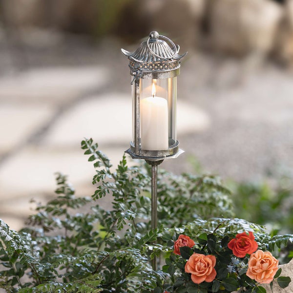 Gartenlaterne mit Kerze auf einem Beet aus Rosen und Farnen