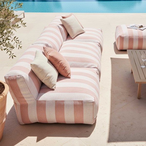 Modernes Outdoor-Loungeset mit gestreiftem Sofa und Hocker auf einer sonnigen Terrasse am Pool, inklusive Kissen und Holztisch.