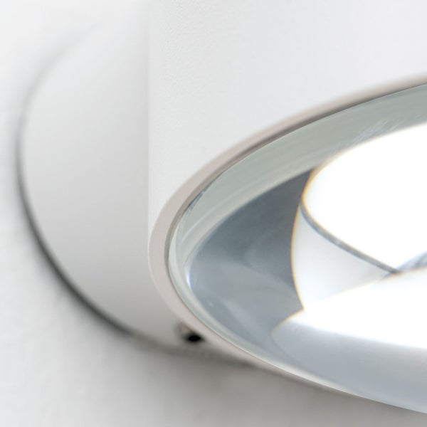 Detailansicht einer modernen weißen Wandleuchte mit gewölbtem Metallgehäuse und Glaslinse.