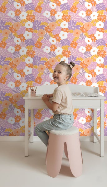 Helle Kinderzimmerszene mit einem Mädchen am weißen Schreibtisch vor einer Vliestapete mit buntem floralem Retro-Muster.