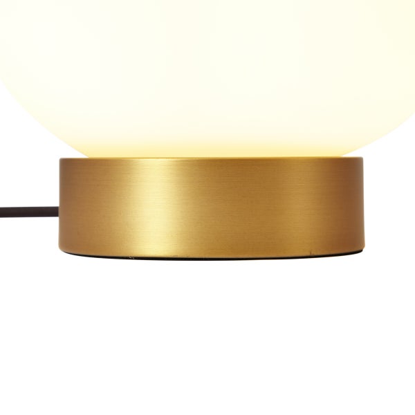 Tischleuchte mit zylindrischem Sockel in Gold-Optik und einer leuchtenden Kugel aus weißem Glas.