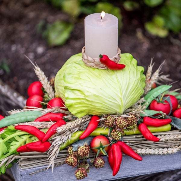 Dekorative Anordnung mit Kohlkopf, Kerze, Chili und Getreideähren.