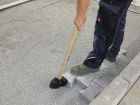 Handwerker richtet Pflastersteine mit einem Pflasterhammer auf einem Splittbett aus