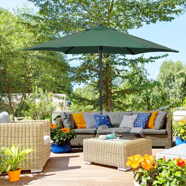 Szene im Garten mit Sonnenschirm, Korbmöbeln und dekorativen Pflanzen.