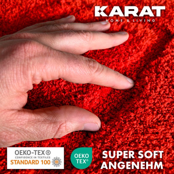 Detailaufnahme eines roten Teppichs mit einer Hand, die die weiche Textur berührt, mit Karat Home and Living Logo und OEKO-TEX Standard 100 Siegel für schadstoffgeprüfte Textilien