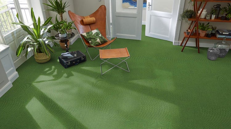 Grüner Teppichfliesen-Bodenbelag in einem hellen Wohnzimmer mit Ledersessel und Zimmerpflanzen.