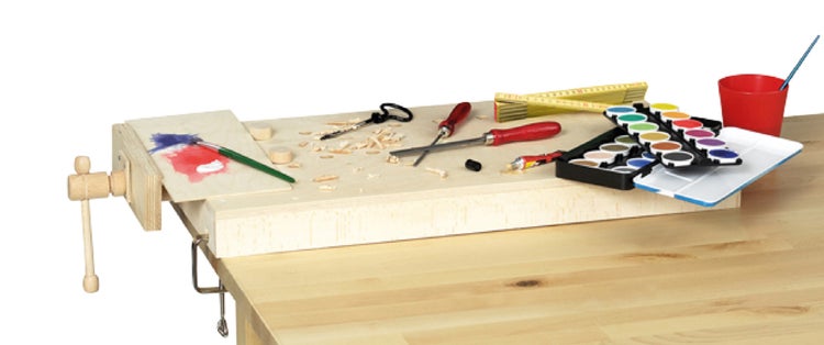 Eine mobile Hobelbank aus Holz mit Schraubstock, auf der Malutensilien, ein Zollstock und Werkzeuge auf einem Tisch arrangiert sind.
