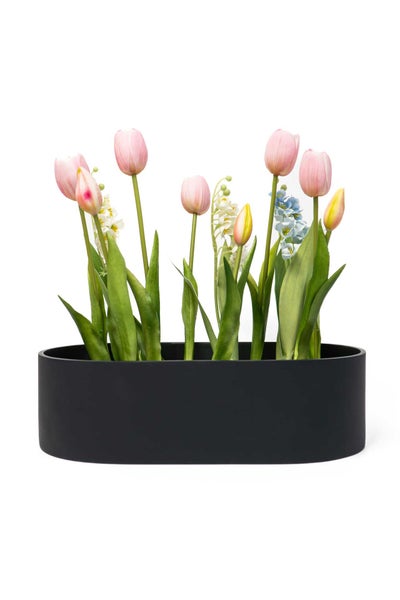 Ovaler schwarzer Pflanzkübel mit künstlichen Blumen wie Tulpen und Maiglöckchen.