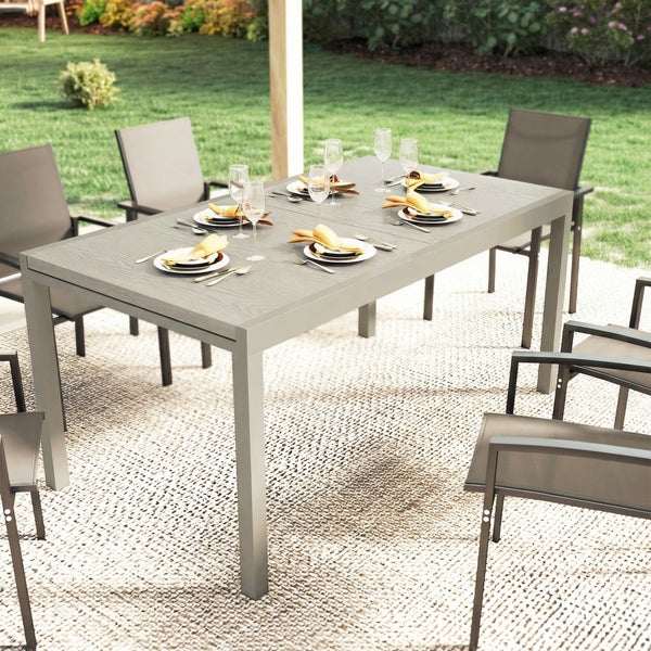 Moderne Garten-Sitzgruppe mit großem rechteckigem Tisch und Stühlen in Holzoptik auf einer hellen Terrasse neben einem Garten.