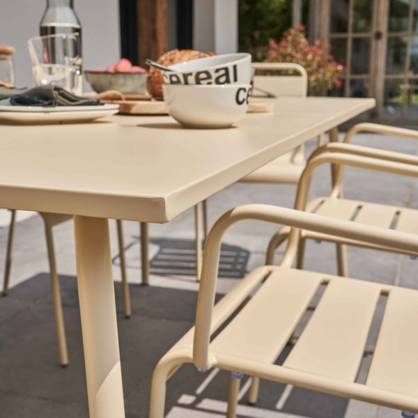 Modernes Gartenmöbel-Set aus beigem Metall mit Tisch und Stühlen auf einer Terrasse, gedeckt zum Frühstück.
