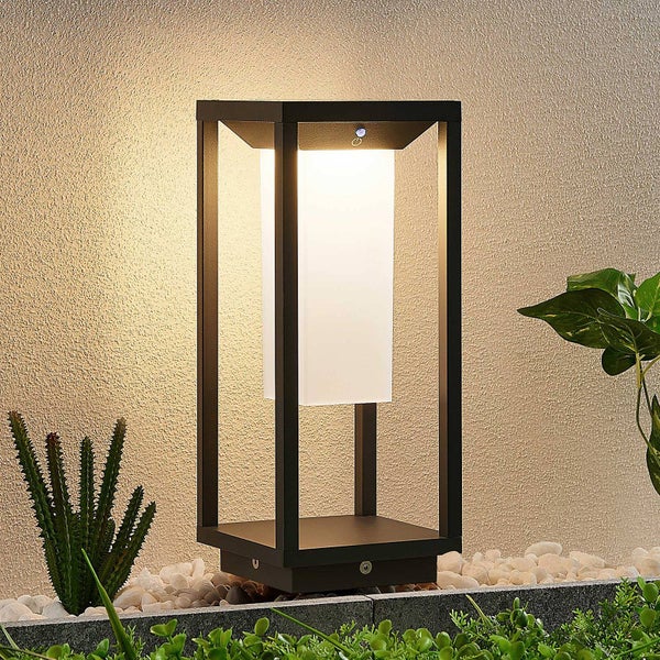 Moderne rechteckige Sockelleuchte für den Außenbereich mit schwarzem Rahmen und weißem Diffusor in einem Beet mit Kieselsteinen.