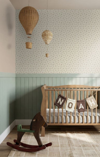 Helles Kinderzimmer mit Babybett aus Holz, grüner Wandvertäfelung, gemusterter Tapete, einem Schaukelpferd und dekorativen Heißluftballons.