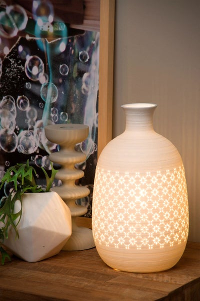 Dekorative Szene mit einer leuchtenden Tischleuchte mit Blumenmuster neben einer Pflanze und einem Kerzenhalter auf einem Tisch