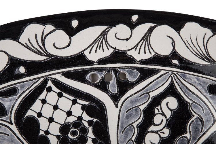 Detailansicht eines Waschbeckens mit floralem Muster und Überlauflöchern.