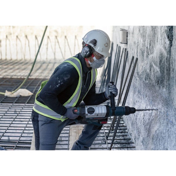 Ein Bauarbeiter bohrt mit einem Bohrhammer in eine Betonwand. Der Arbeiter trägt Schutzkleidung.