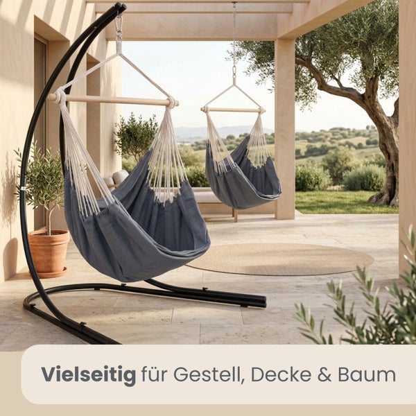 Grauer Hängesessel aus Stoff mit Holzstab, präsentiert auf einem schwarzen Metallgestell und hängend an der Decke auf einer hellen Terrasse.
