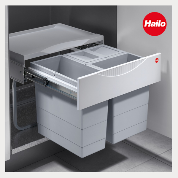 Hailo Mülltrennsystem für Küchenunterschränke, ausziehbar mit zwei grauen Abfalleimern und integrierter Ablagefläche. Hailo Logo.