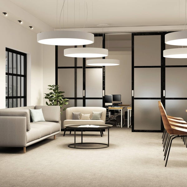 Moderne Bürolandschaft mit mehreren runden, flachen LED-Pendelleuchten über Sofas, einem Couchtisch und gläsernen Raumteilern.