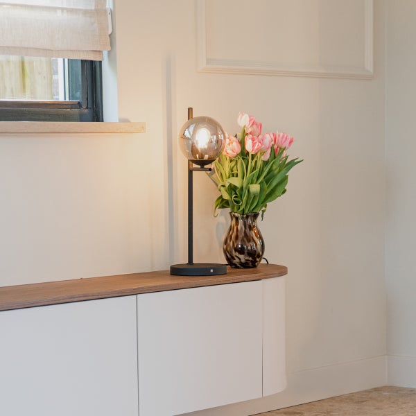 Dekorative Tischleuchte mit runder Glaskugel und Blumen in einer Vase auf einem Schrank