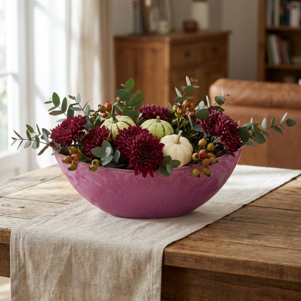 Dekorative Schale mit herbstlichem Gesteck aus Chrysanthemen, Zierkürbissen und Eukalyptuszweigen auf einem Holztisch.
