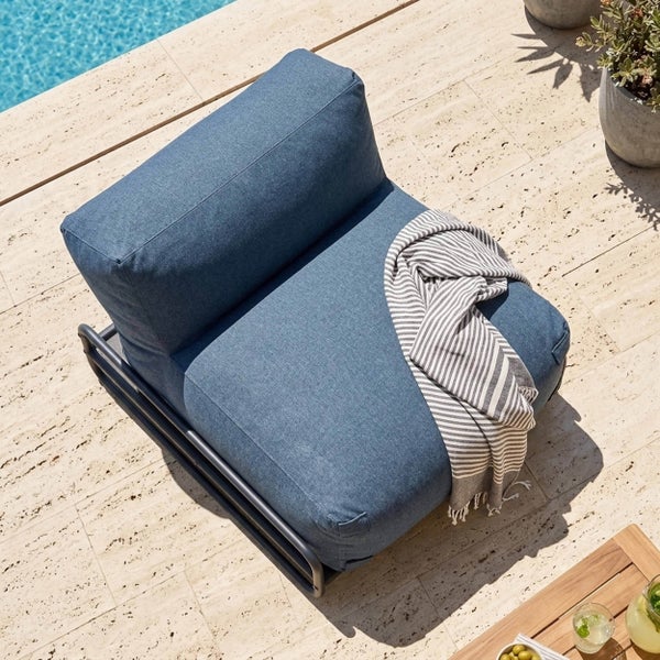Loungesessel mit blauen Polstern und dunklem Metallgestell auf einer Steinterrasse am Pool, dekoriert mit einer gestreiften Decke.