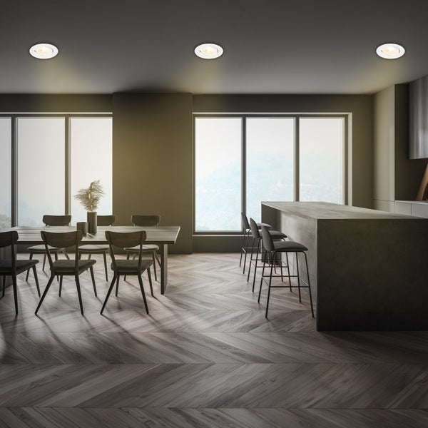 Modernes Esszimmer mit runden Einbaustrahlern an der Decke, Holztisch, Stühlen, Kücheninsel und Boden in Fischgrätoptik.
