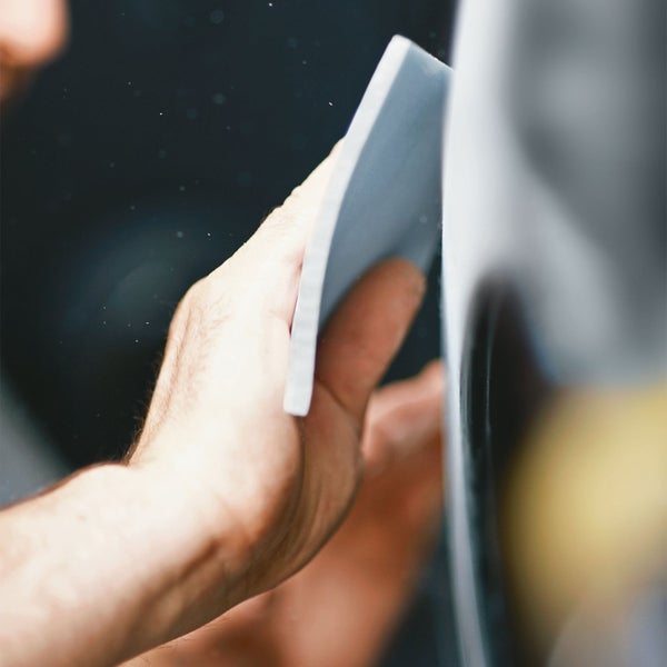 Nahaufnahme einer Person, die eine Oberfläche mit Schleifpapier bearbeitet